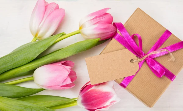 Día de las madres. Tulipanes rosados y un regalo de tarjeta en blanco sobre fondo blanco, vista superior, espacio para copiar — Foto de Stock