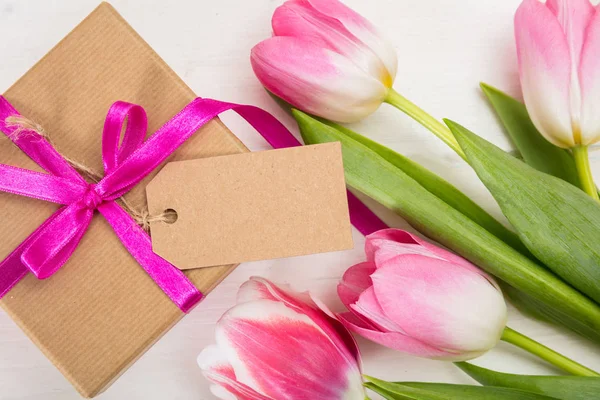 Día de las madres. Tulipanes rosados y un regalo de tarjeta en blanco sobre fondo blanco, vista superior, espacio para copiar — Foto de Stock