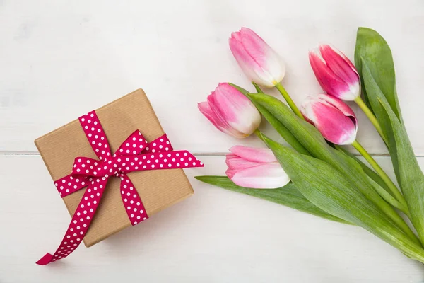 Dia das mulheres. Tulipas rosa e um presente no fundo branco, vista superior — Fotografia de Stock