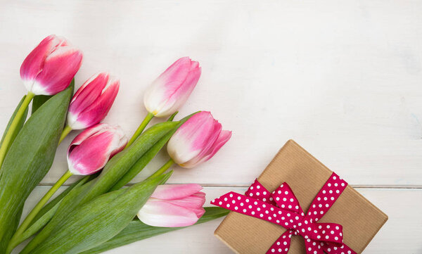 Women's day. Pink tulips and a gift on white background, top view