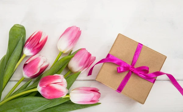 Dag van de vrouw. Roze tulpen en een gift op witte achtergrond, bovenaanzicht — Stockfoto