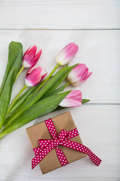 Women's day. Pink tulips and a gift on white background, top view