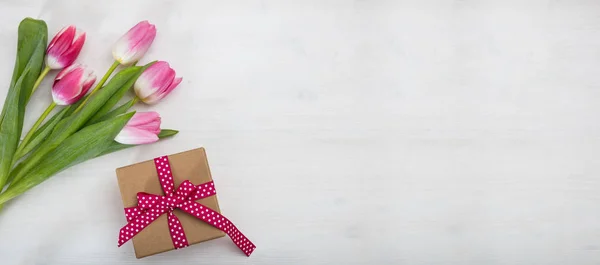 Dia das mulheres. Tulipas cor-de-rosa e um presente no fundo branco, banner, vista superior, copyspace — Fotografia de Stock
