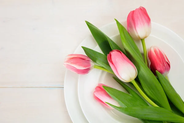 Pink tulips on white plates, white wooden background. Top view — Stock Photo, Image