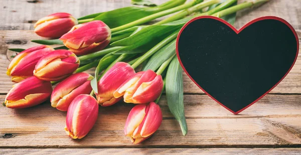 Tulpen en een lege hart vorm board op houten achtergrond, kopie ruimte — Stockfoto