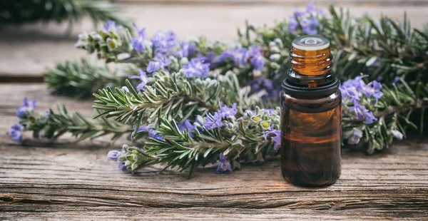 Ätherisches Rosmarinöl und frisch blühender Zweig auf einem Holztisch, Nahaufnahme — Stockfoto