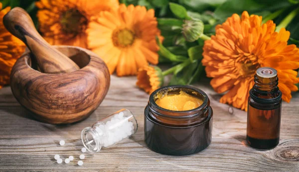 Natural medicine. Essential oil, ointment a mortar and white pills on a wooden table, fresh blooming calendula background, — Stock Photo, Image