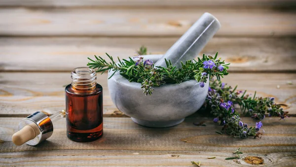 Olio essenziale di rosmarino e ramoscello fresco in fiore in un mortaio, tavolo di legno — Foto Stock