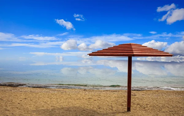 Wooden umbrella on an empty sandy beach. Blue sky and calm sea background. — Stock Photo, Image