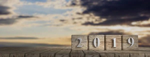 Ano Novo 2019 em cubos de madeira, mesa de madeira, fundo do nascer do sol, banner, espaço de cópia. ilustração 3d — Fotografia de Stock