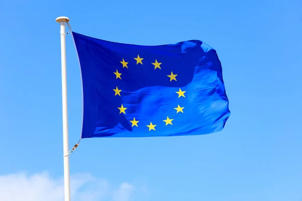 Flaga UE. Flaga Unii Europejskiej na słupie macha na tle niebieskiego nieba — Zdjęcie stockowe