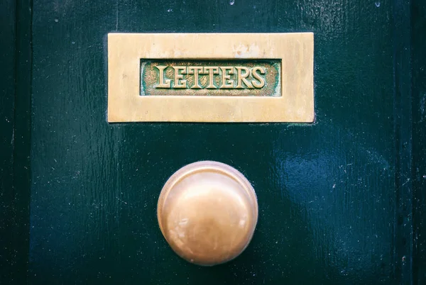 Vecchia cassetta postale in ottone e manopola su una porta d'ingresso dipinta di verde, lettere di testo — Foto Stock