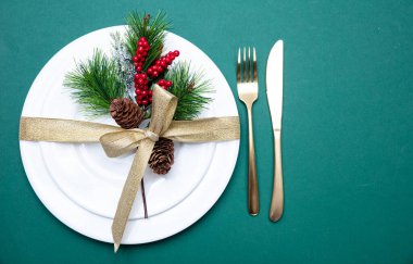 Xmas yeri ayarı. Altın çatal bıçak takımı ve beyaz tabak takımı, yeşil arka plan.