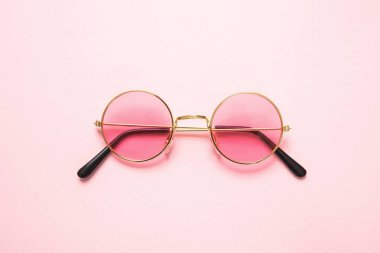 Pembe arka planda pembe lensli altın çerçeveli güneş gözlüğü.