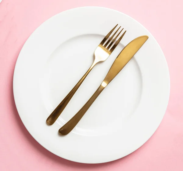 Talheres de ouro e pratos definidos contra fundo rosa, local formal — Fotografia de Stock