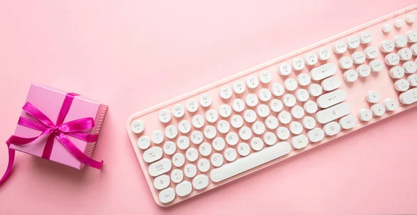 Christmas gift and computer keyboard against pink background