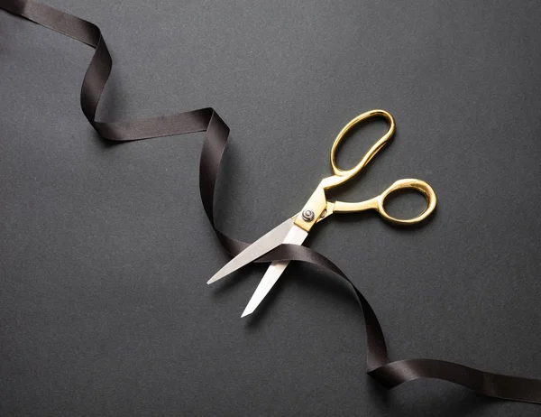 Открытие. Золотые ножницы, перерезающие черную атласную ленту, черный фон — стоковое фото