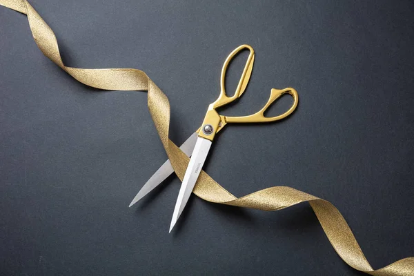 Открытие. Золотые ножницы, перерезающие золотую атласную ленту, черный фон — стоковое фото