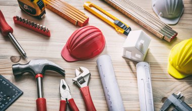 Aletler, kasklar ve proje planları ahşap masada.