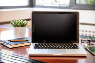 Ahşap bir masanın üstünde siyah, boş ekranlı bir laptop.