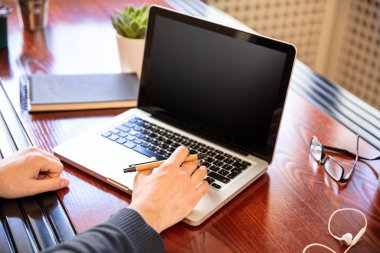 Ahşap bir masanın üstünde siyah, boş ekranlı bir laptop.