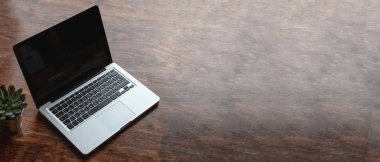 Ahşap bir masanın üstünde siyah, boş ekranlı bir laptop.