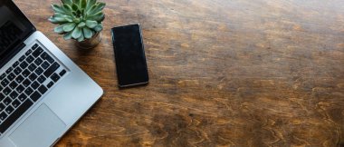 İş yeri. Bilgisayar dizüstü bilgisayarı ve cep telefonu ahşap ofis masasında, üst görünümde.