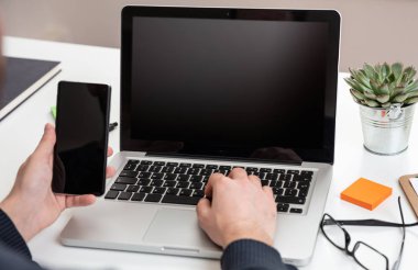 Laptop ve siyah boş ekranlı akıllı telefon, ofis içi arka plan