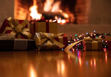 Noel hediyeleri ve ışıklar parlıyor, yanan şömine arka planı bulanıklaşıyor.