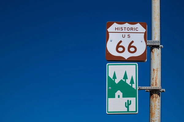 Straßenschilder der historischen Route 66 und einsame Straße mit Wüste, Bergen und Kakteen. Flagstaff, arizona, us. — Stockfoto