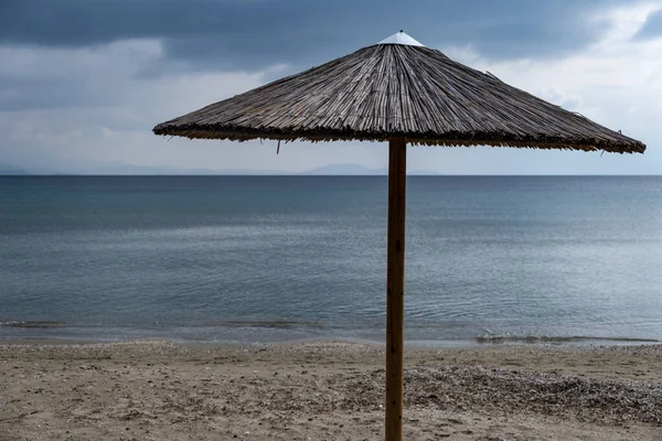 Szalma esernyő egy üres homokos tengerparton. Sötétkék tenger és ég háttér — Stock Fotó