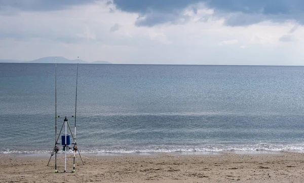 Két horgászbot egy üres homokos tengerparton várja a halat. Bolyhos felhők háttér, tér. — Stock Fotó