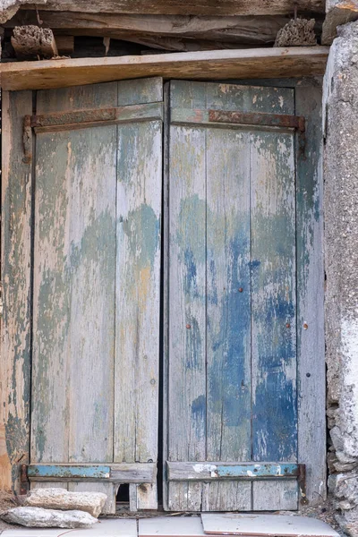 Vieux volets doubles fermés en bois. Des charnières rouillées sur des planches pelées, des pierres gardent la fenêtre fermée. Vue verticale . — Photo