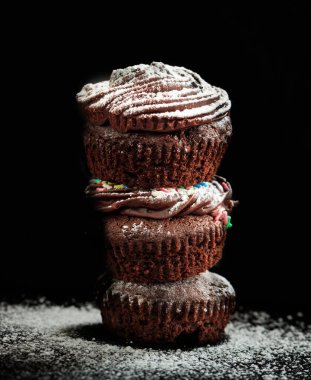 Siyah arka planda pudra şekerle süslenmiş bir yığın çikolatalı kek. Keklerin dikey portresi. Kutlamalar için mükemmel tatlı yiyecekler..