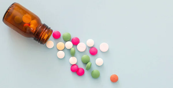 Medicine pills scattered out of a glass bottle on blue background. Pharmacy pills top view. Medical treatment, health concept