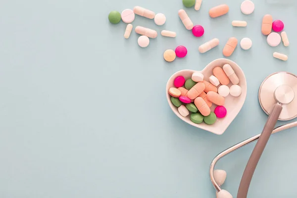 Heart disease treatment. Pills, tablets capsules and stethoscope on blue pastel background. Colorful variation of pharmacy products, top view. Medical treatment, health concept