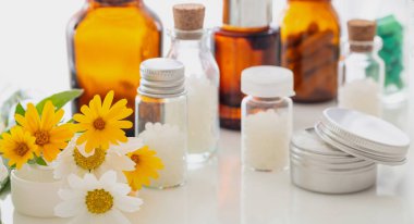 Alternatif bitkisel ilaç. Taze sarı papatyalar, homeopatik küreseller, esensial yağ ve beyaz arka plana karşı merhem. Homeopati, doğal ürünler konsepti