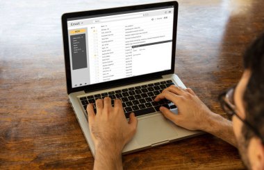 Bir bilgisayar ekranındaki e-posta kutusu mesaj listesi, dizüstü bilgisayarla çalışan bir adam, ahşap ofis masası geçmişi, iş yeri ofis kavramı. E-posta yazışma konsepti