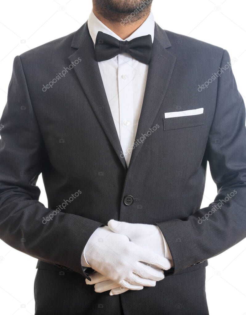 Butler, waiter with blue black color tuxedo and bow tie, folded hands with gloves, ready to serve, standing on white background. Vertical portrait.