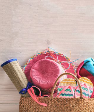 Yaz kumsalı çantası ve pembe ahşap arka planda aksesuarlar. Hasır şapka, terlik, güneş gözlüğü ve havlu. Dikey fotoğraf, boşluğu kopyala.