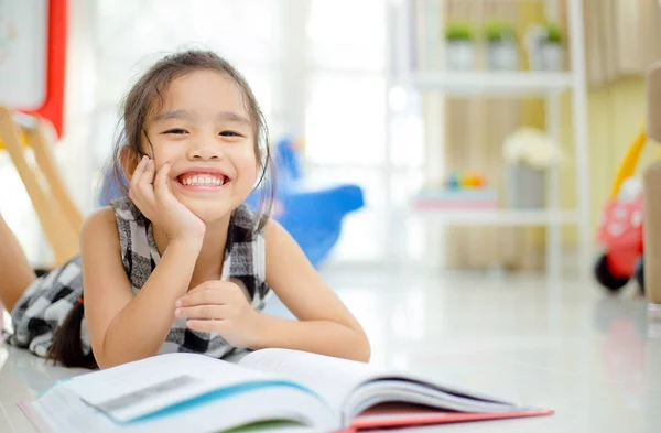 Carino asiatico ragazza lettura un libro e sorridente denti bianco mentre in il vivere stanza . — Foto Stock