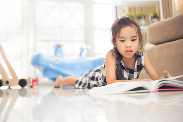 Linda chica asiática leyendo un libro mientras está en la sala de estar . — Foto de Stock