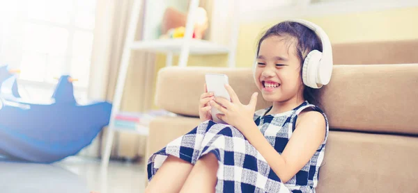 Szczęśliwa dziewczyna azjatyckich za pomocą słuchawki słuchać muzyki przez smartfon w sali na żywo — Zdjęcie stockowe
