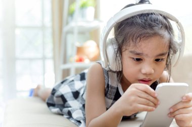 Yanında smartphone canlı odada dinlemek müzik için kulaklık kullanarak mutlu Asyalı kız