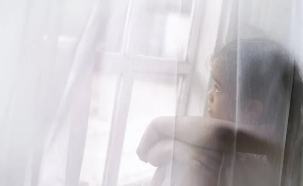 Депрессивная маленькая девочка у окна дома — стоковое фото
