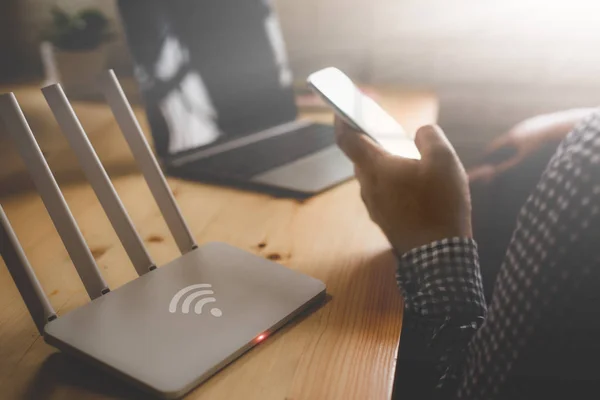 Primer plano de un router inalámbrico y un hombre que utiliza el teléfono inteligente en la sala de estar —  Fotos de Stock