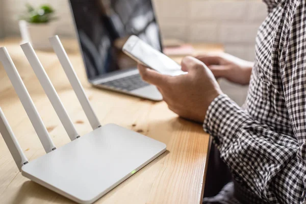 Primer plano de un router inalámbrico y un hombre que utiliza el teléfono inteligente en la sala de estar —  Fotos de Stock