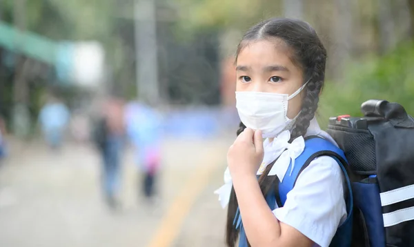 Pequeña chica asiática usando una máscara protectora en la escuela —  Fotos de Stock