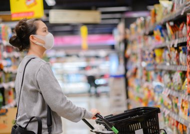 Süpermarkette maske takan Asyalı bir kadın, Coronavirus covid-19 pandemisi sırasında panik alışverişi yapıyor. Malzeme deposundan bütçe alımı.