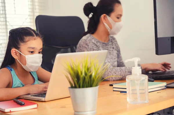 mom working at home wearing protective mask  with her child on the table while writing an report. woman working from home, while in quarantine isolation during the Covid-19 health crisis